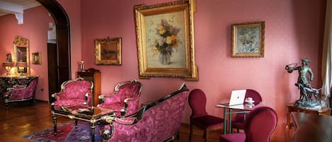 A room with a wooden floor, pink walls, and a large painting of flowers. There are two chairs, a table, and a statue.