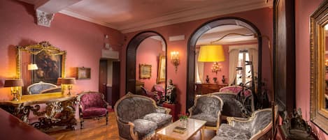 A room with ornate furniture, including a chaise lounge and armchairs, a wooden coffee table, and a piano.