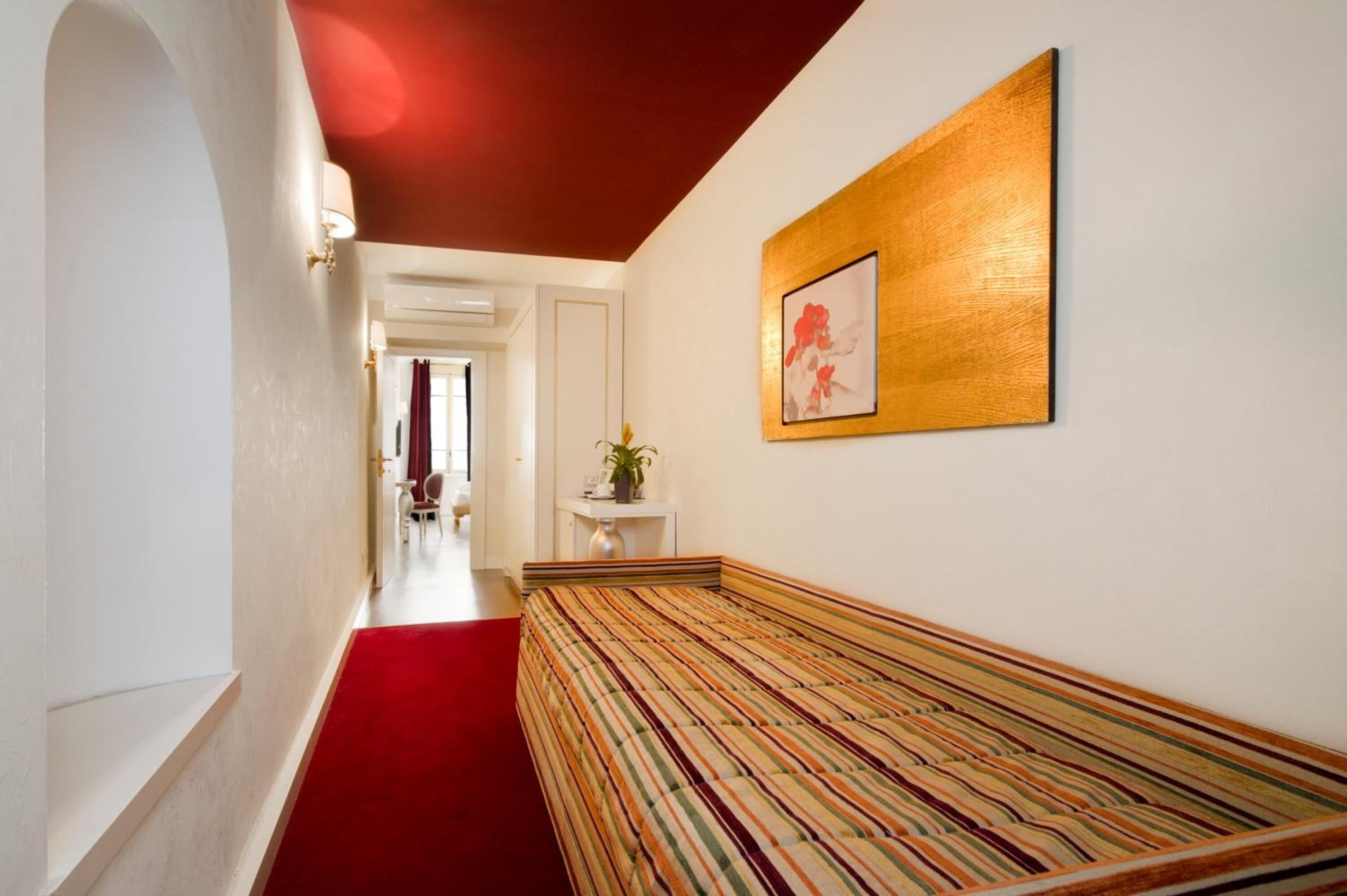 Un pasillo con alfombra roja, un banco y una obra de arte enmarcada en la pared.