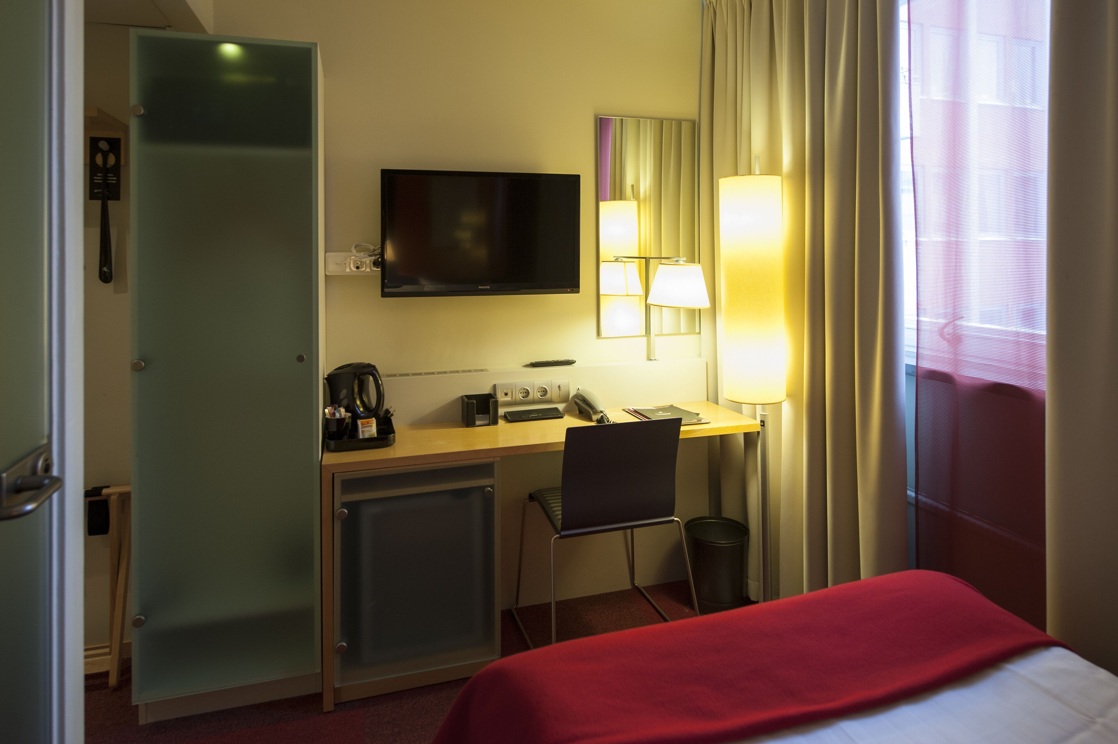 Una habitación de hotel con una cama, un escritorio con computadora, un televisor y una ventana con cortinas.