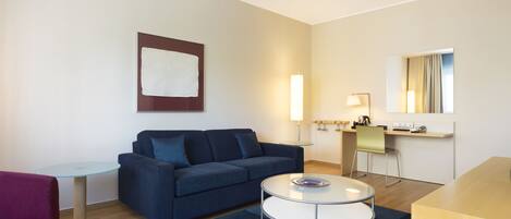 A modern living room with a blue sofa, a glass coffee table, a small round table, and a large mirror.