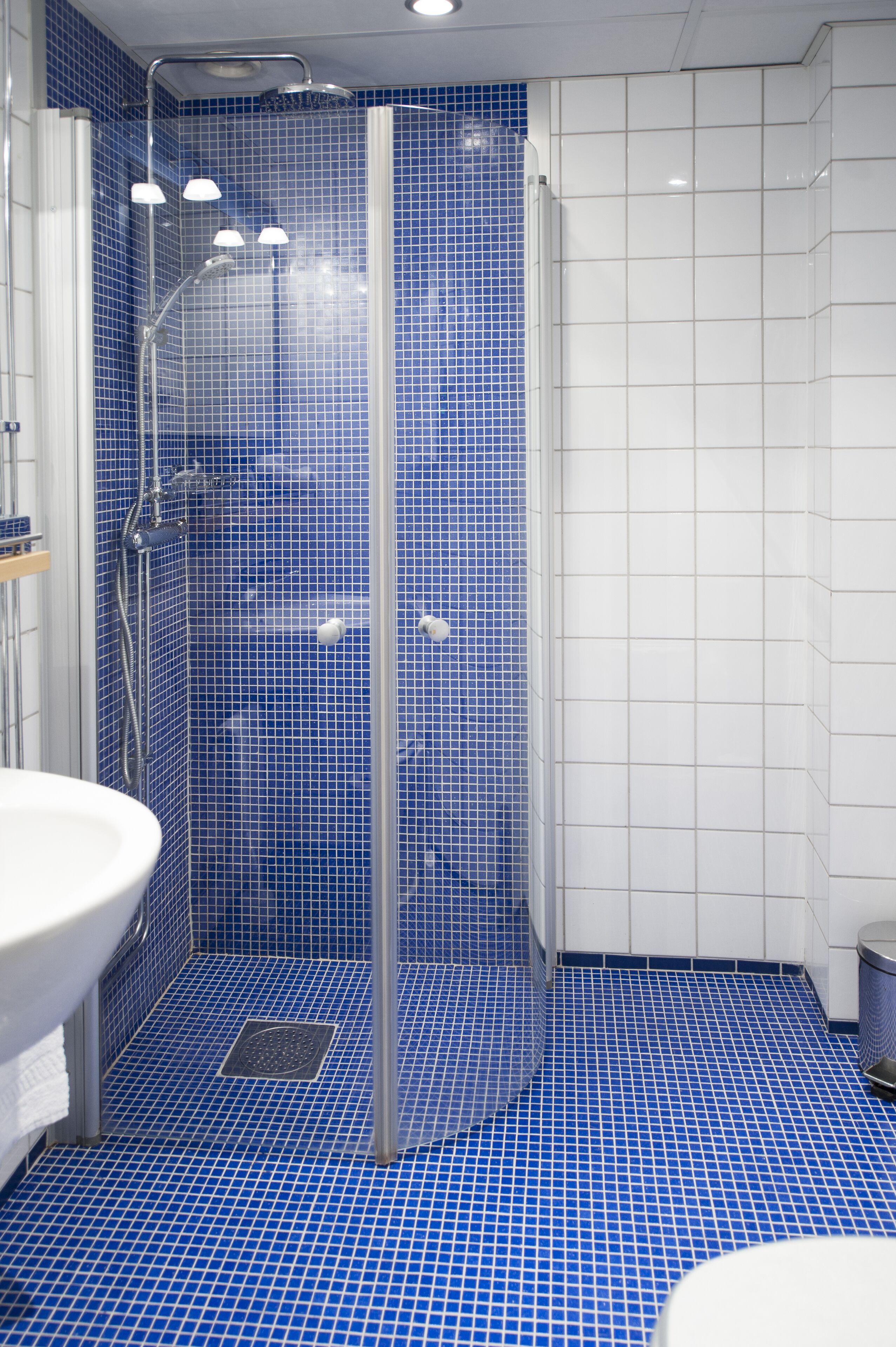 Un baño con cabina de ducha con azulejos azules, un lavamanos blanco y un inodoro blanco.