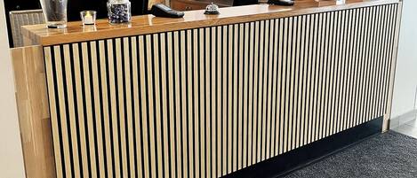 Un mostrador de recepción con detalles de madera, piso cubierto de alfombra negra y un techo moderno con iluminación empotrada.