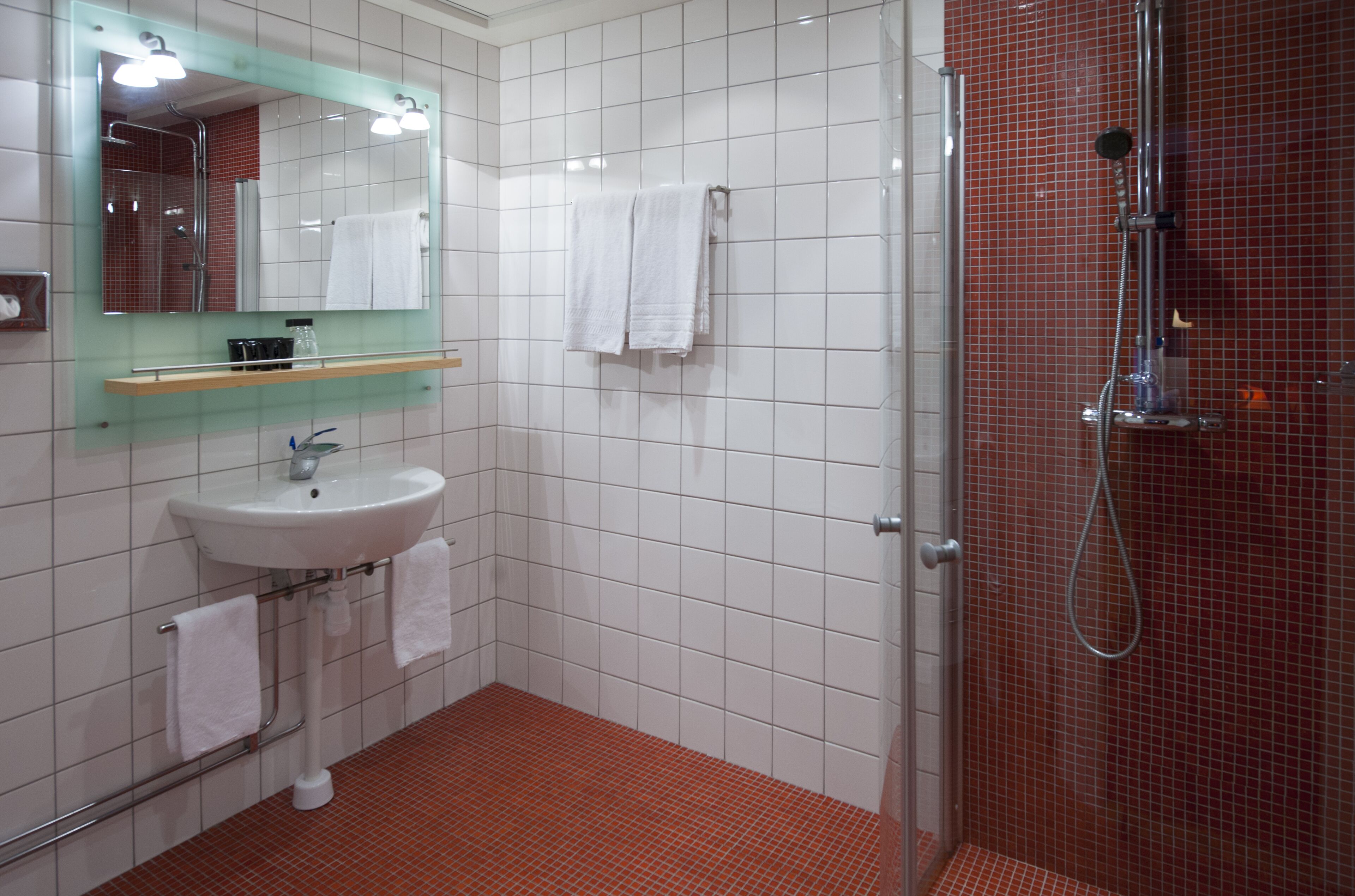 A bathroom with a white sink, a mirror, a shower, and a tiled floor.