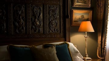 Een slaapkamer met een houten hoofdbord, een bed met blauwe en beige kussens, een staande lamp en ingelijste foto's aan de muur.