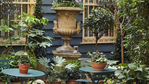 An outdoor patio area with green tables and chairs, surrounded by potted plants and a large decorative urn. - The Rookery Hotel (London)