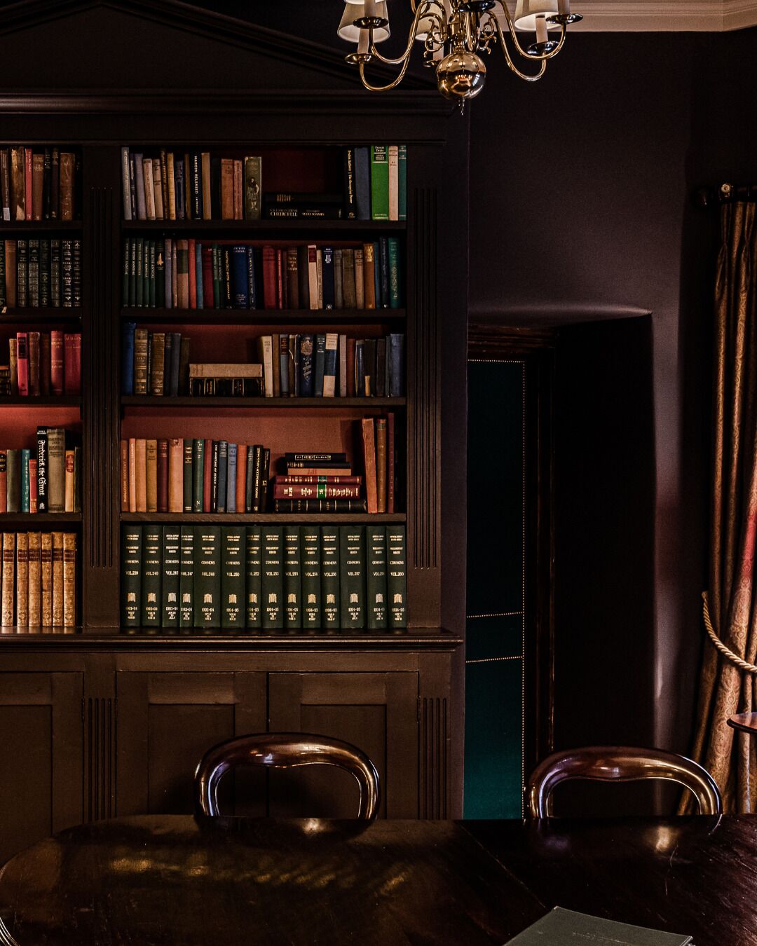 A library with bookshelves, a chandelier, and two chairs.