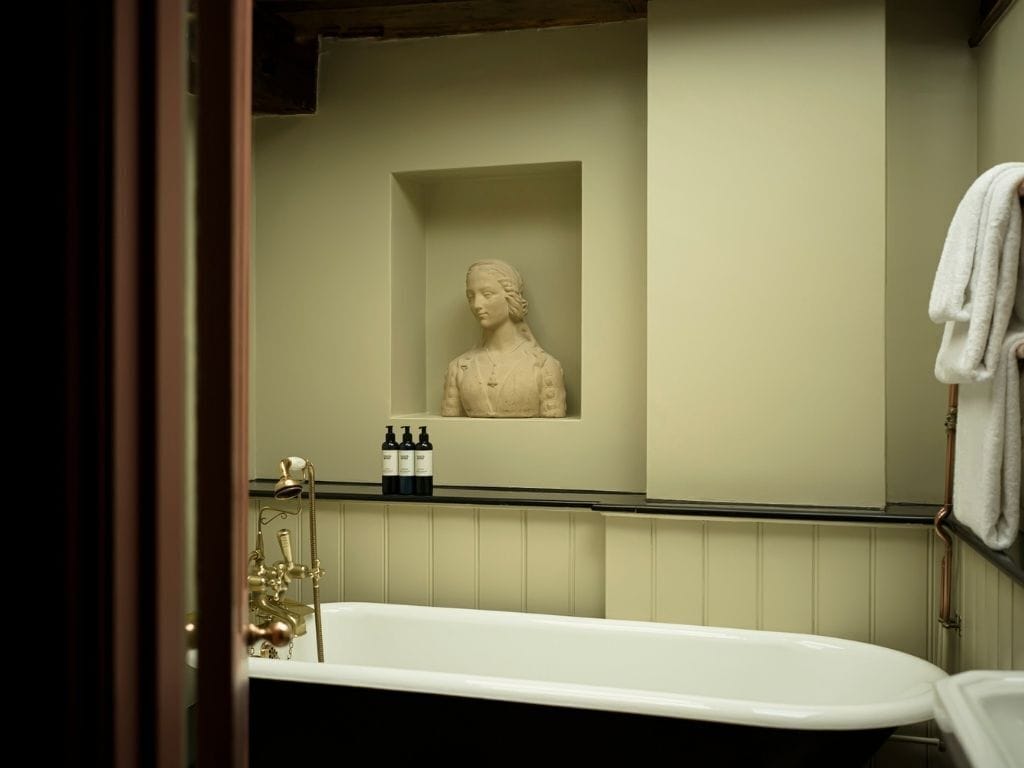 Un baño con una bañera, una escultura en la pared y artículos de aseo en la estantería.