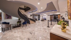 A modern lobby with a curved staircase, marble flooring, and contemporary furniture. - Hotel Malibu (Zapopan)