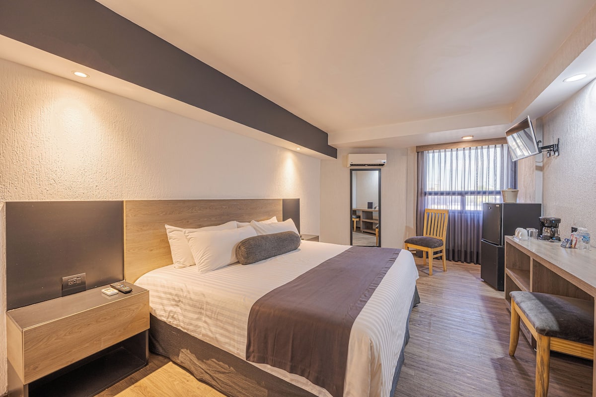 Una habitación de hotel moderna con una cama grande, una mesita de noche y una pequeña zona de escritorio.
