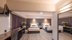 A hotel room with two beds, a desk, and a chair. There is a mirror on one wall and a window with curtains. - Hotel Malibu (Zapopan)