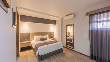 Een moderne hotelkamer met een groot bed, nachtkastjes, een spiegel en een raam met gordijnen.