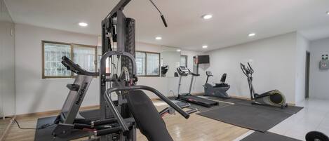 A gym with cardio machines, weightlifting equipment, and a bench.