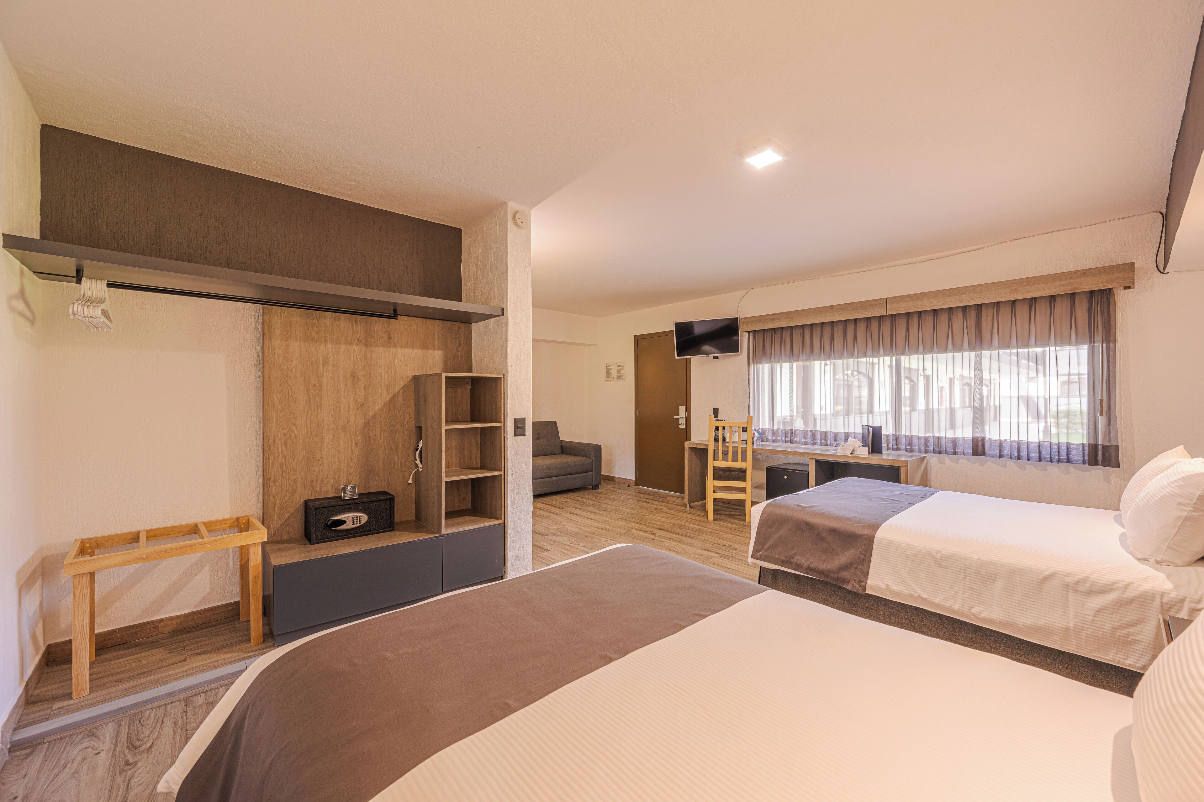 Una habitación de hotel moderna con dos camas, un escritorio, un televisor y un ventanal con cortinas.