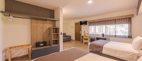 Una habitación de hotel moderna con dos camas, un escritorio, un televisor y un ventanal con cortinas.
