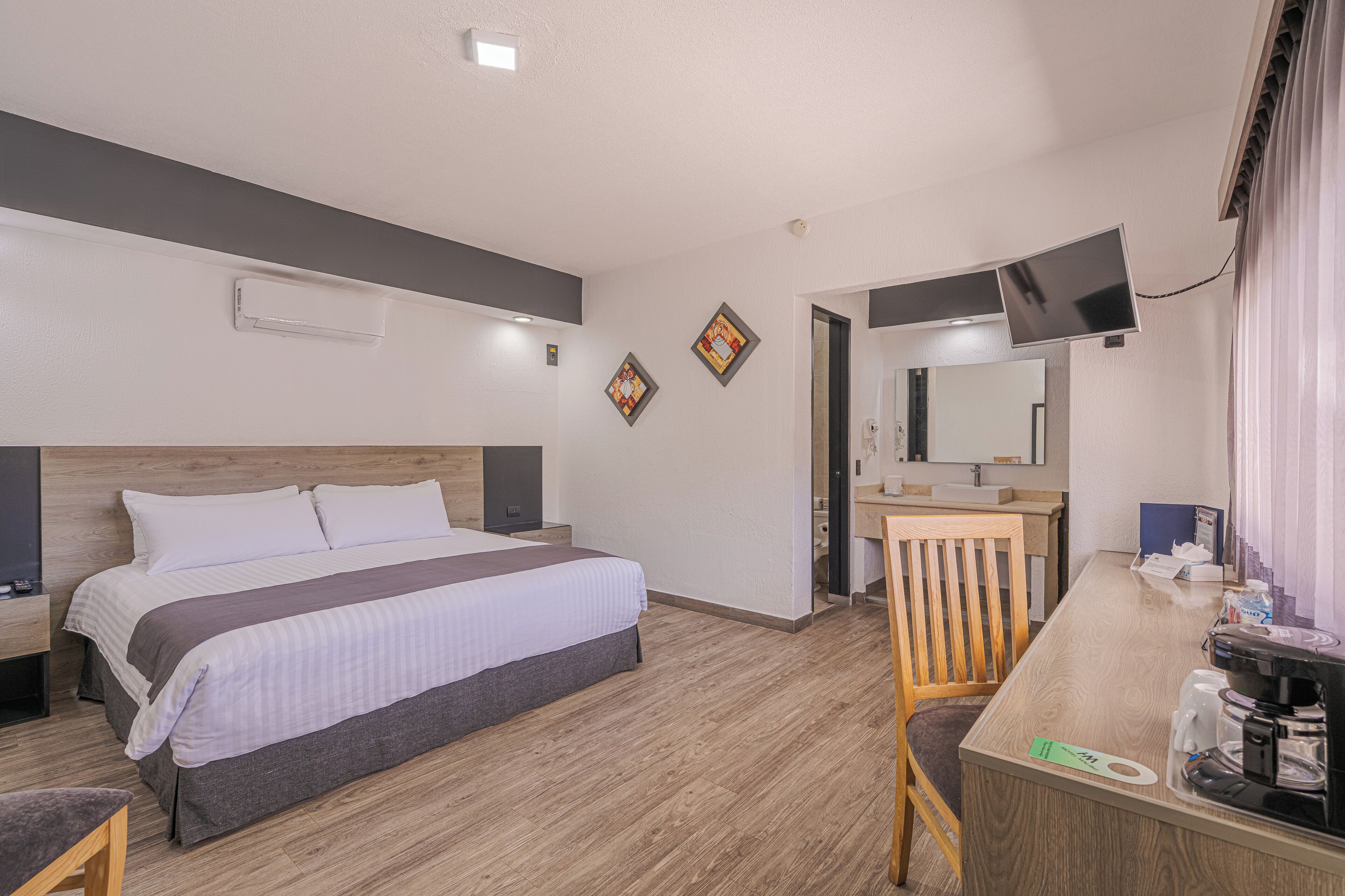 Ein Hotelzimmer mit Bett, Schreibtisch mit Kaffeemaschine, Spiegel und Wandfernseher.