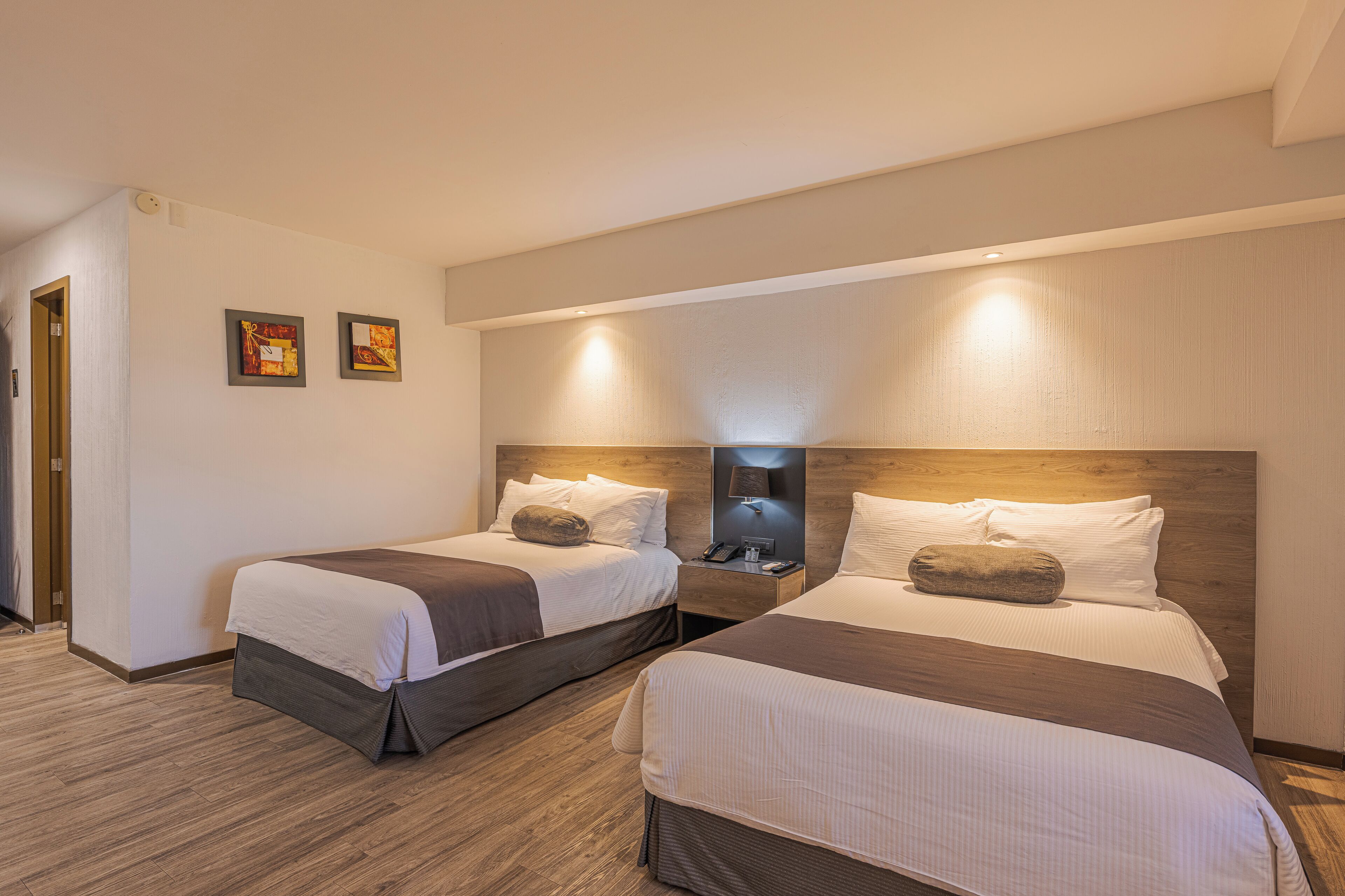 Ein Hotelzimmer mit zwei Betten, Holz-Kopfteilen, Nachttischen mit Lampen und einer Tür zu einem weiteren Raum.