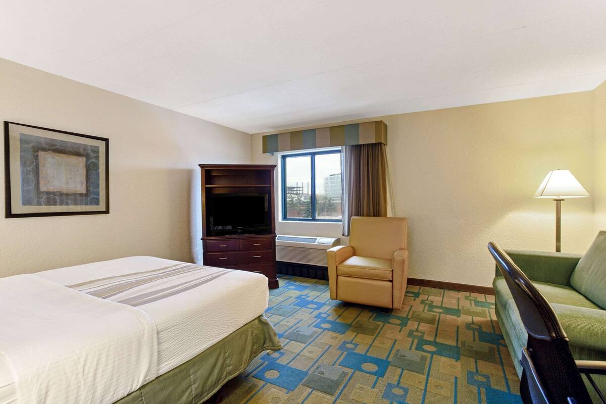 Een hotelkamer met een bed, een bureau, een stoel, een televisie en een raam met gordijnen.