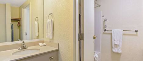 A bathroom with a sink, mirror, towel rack, and shower area.