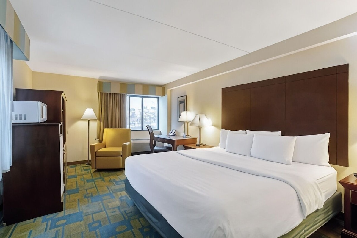 A hotel room with a large bed, a desk, a chair, a wardrobe, and a window with curtains.