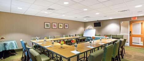 A conference room with a long table, chairs, a projector screen, and an exit door.