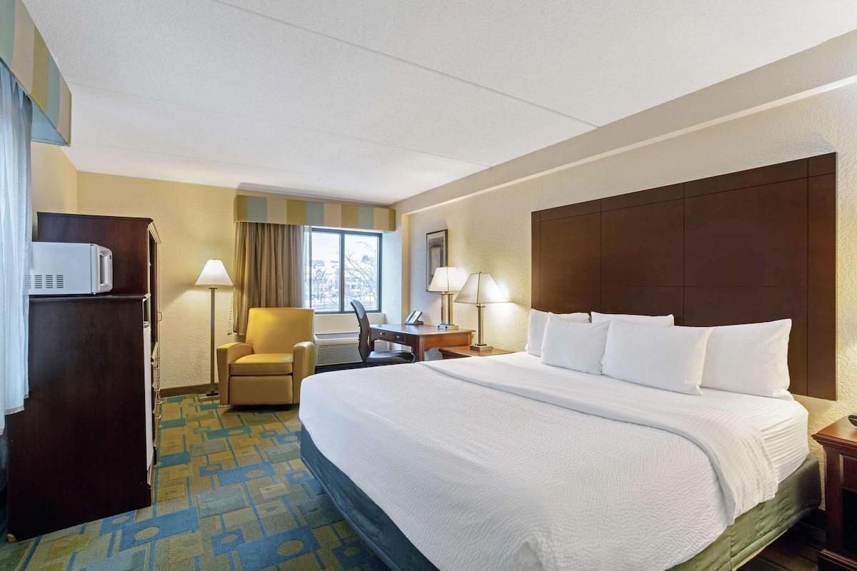 Een hotelkamer met een groot bed, een bureau met stoel, een lamp en een koelkast.