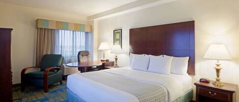 A hotel room with a large bed, a desk, a chair, and two bedside lamps.