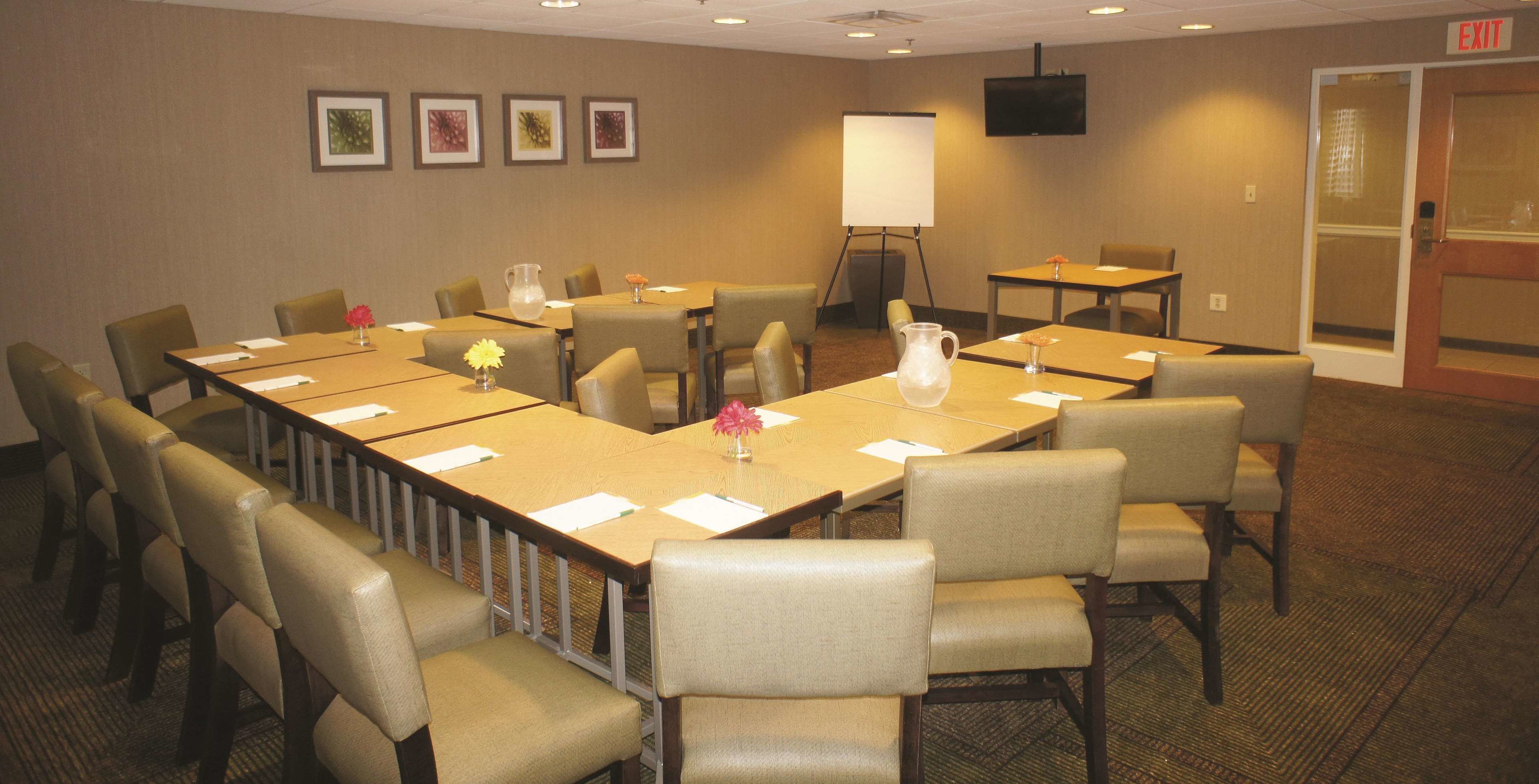 A conference room with a long table, multiple chairs, a whiteboard, and a TV on the wall.