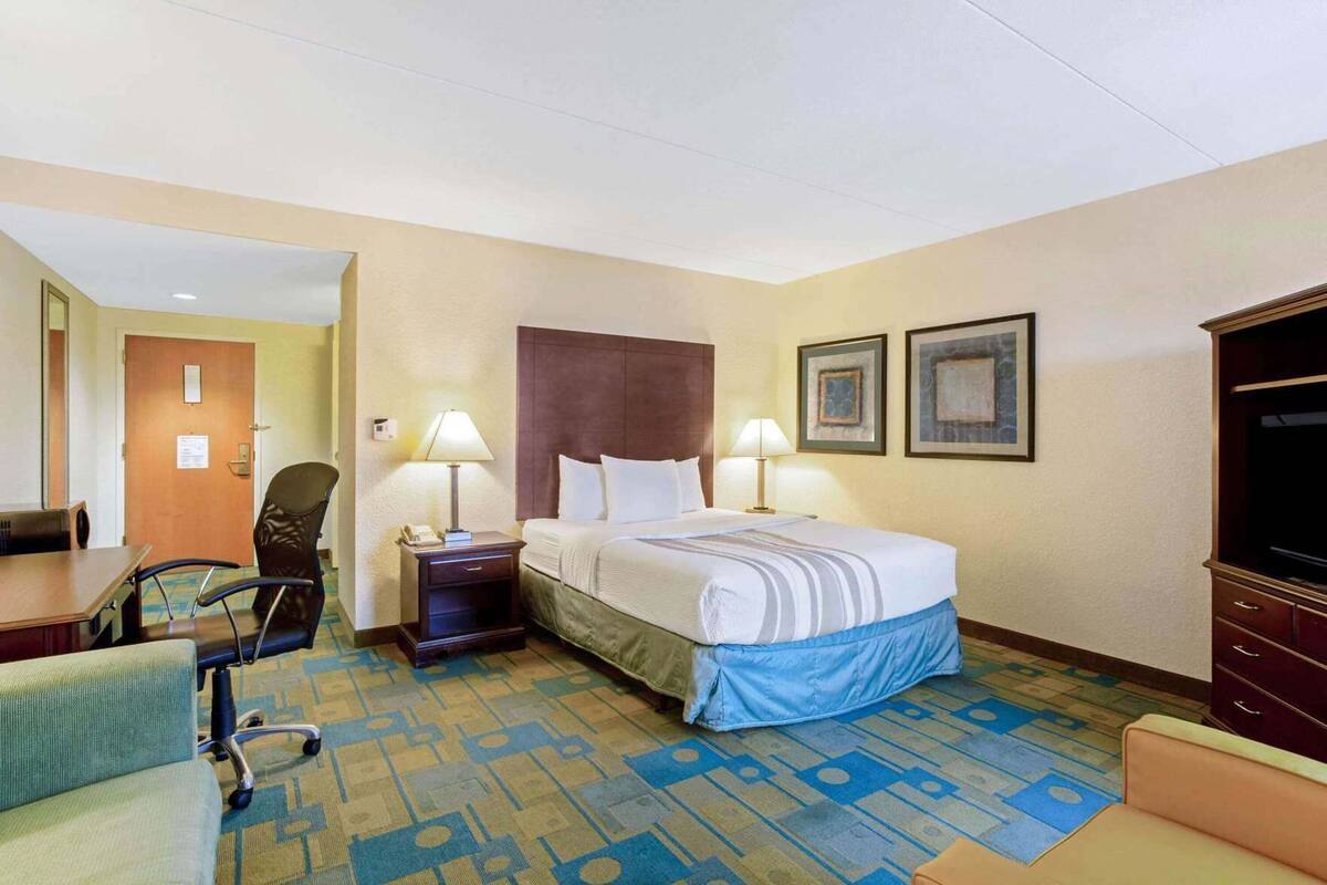 Een hotelkamer met een bed, een bureau, een stoel, een televisie en een tapijtvloer.