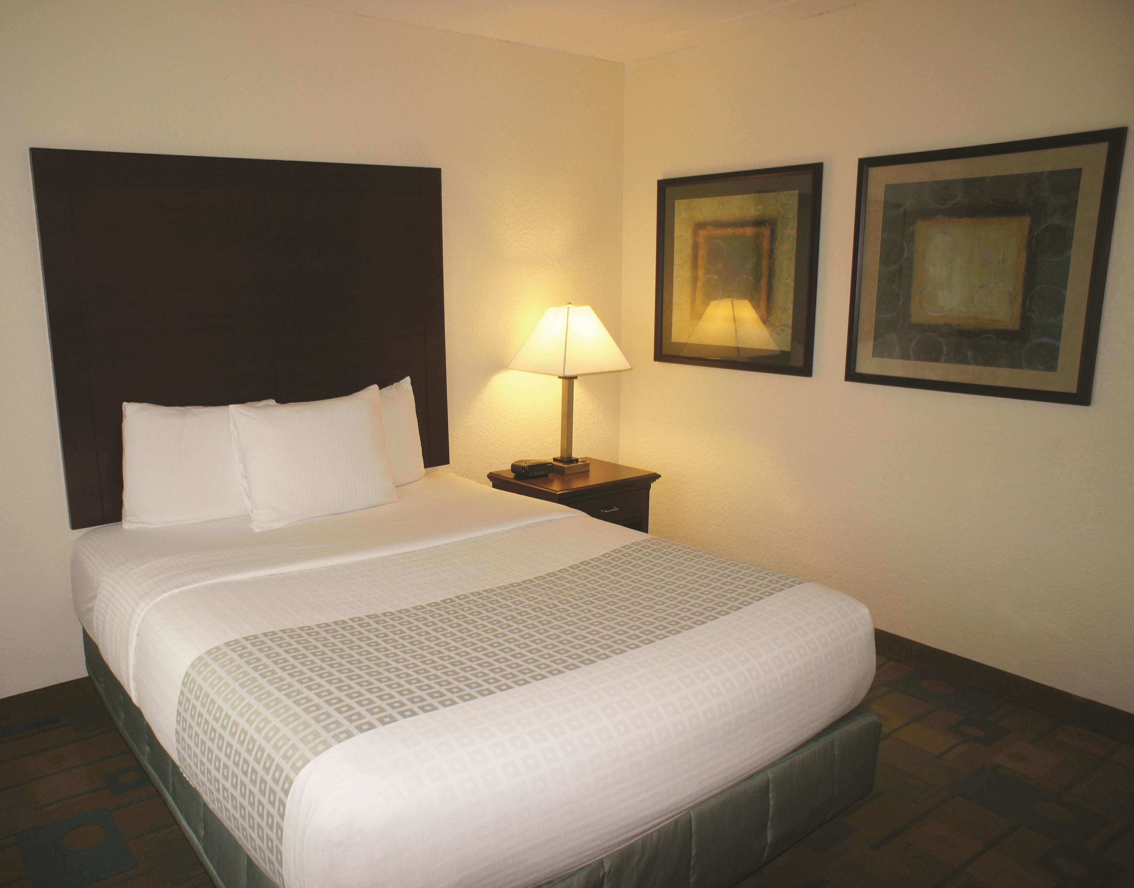 A neatly made bed with white linens and a patterned blanket, a bedside lamp, and two framed artworks on the wall.