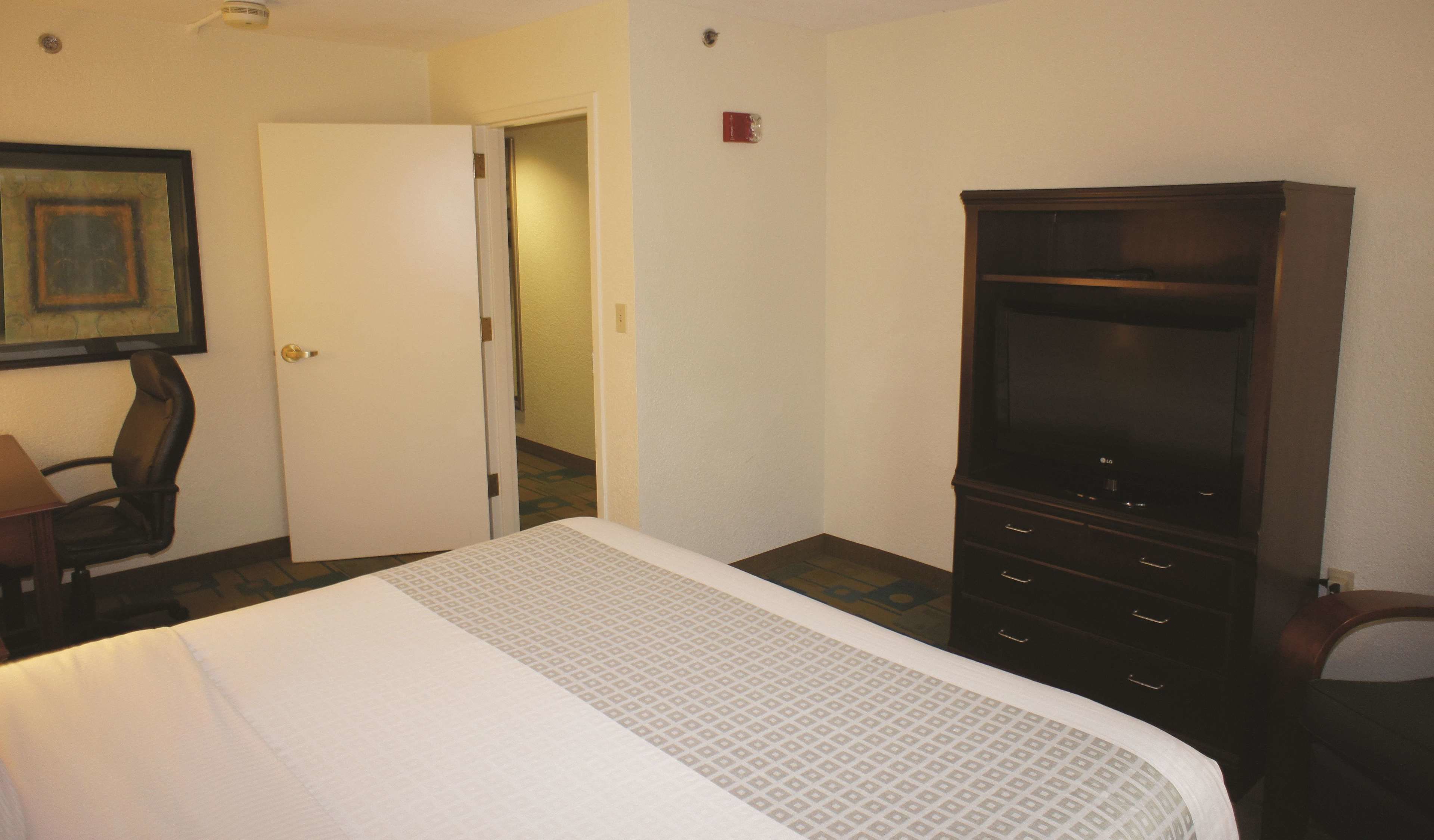 A hotel room with a bed, a TV, a desk, and a door leading to another room.