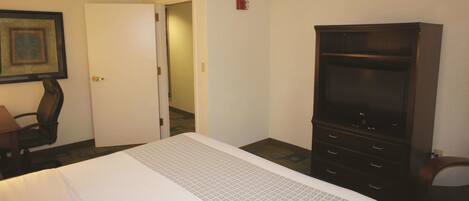 A hotel room with a bed, a TV, a desk, and a door leading to another room.