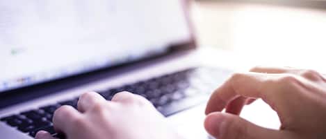 Nahaufnahme von Händen, die auf einer Laptop-Tastatur tippen.