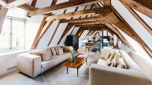 A spacious loft with high ceilings and exposed wooden beams. It features a large sofa, a coffee table, and a dining area with chairs. - The Dylan Amsterdam (Amsterdam)
