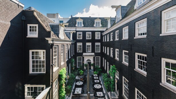 A courtyard with a central pathway, surrounded by black brick buildings with white window frames and a central entrance. - The Dylan Amsterdam (Amsterdam)