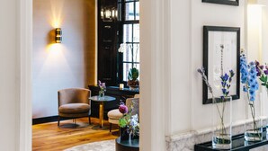 A modern hotel lobby with a round marble floor, a black console table with vases, and a seating area with a chair and a small table. - The Dylan Amsterdam (Amsterdam)
