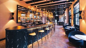 A bar area with a long counter, multiple stools, and hanging lights. - The Dylan Amsterdam (Amsterdam)