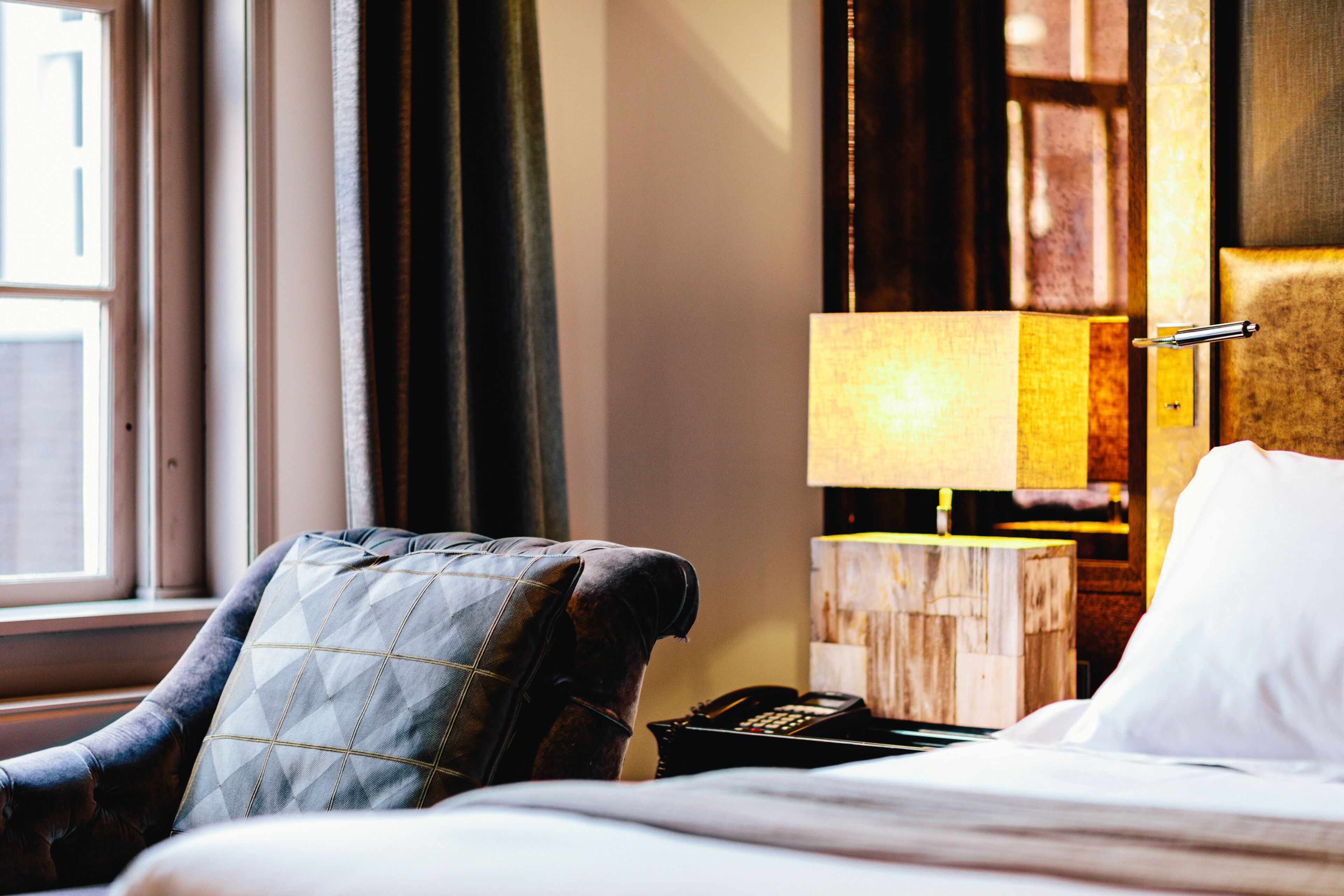 Una camera d'albergo con un letto, una sedia, un comodino con una lampada e un telefono.