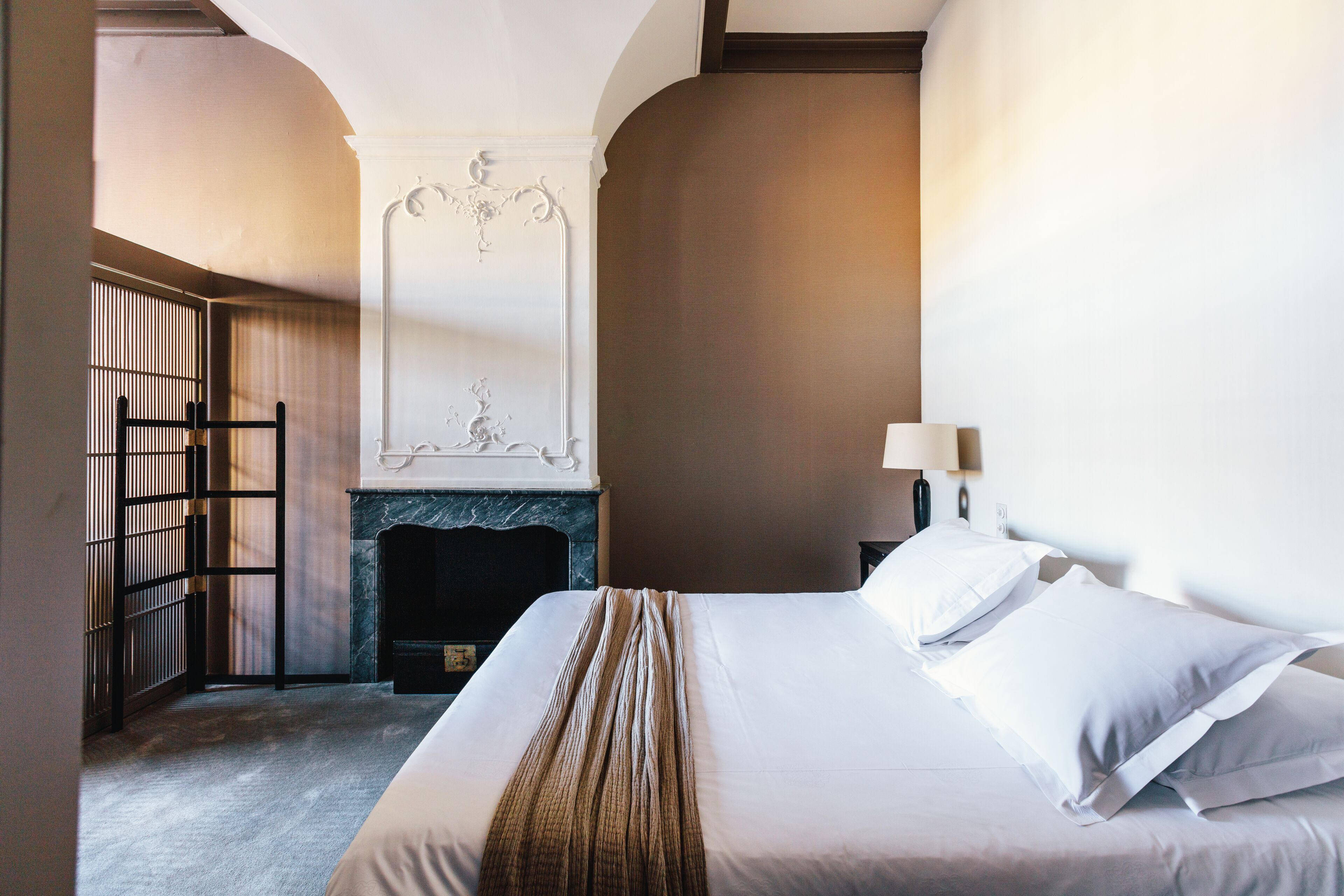 Quarto de hotel com cama, lareira, mesa de cabeceira e abajur.