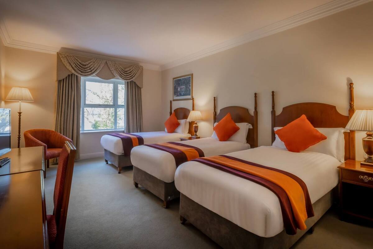 A hotel room with two beds, a desk, a chair, and a window with curtains.