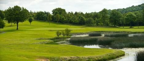 A golf course with a pond, trees, and a hilly landscape.