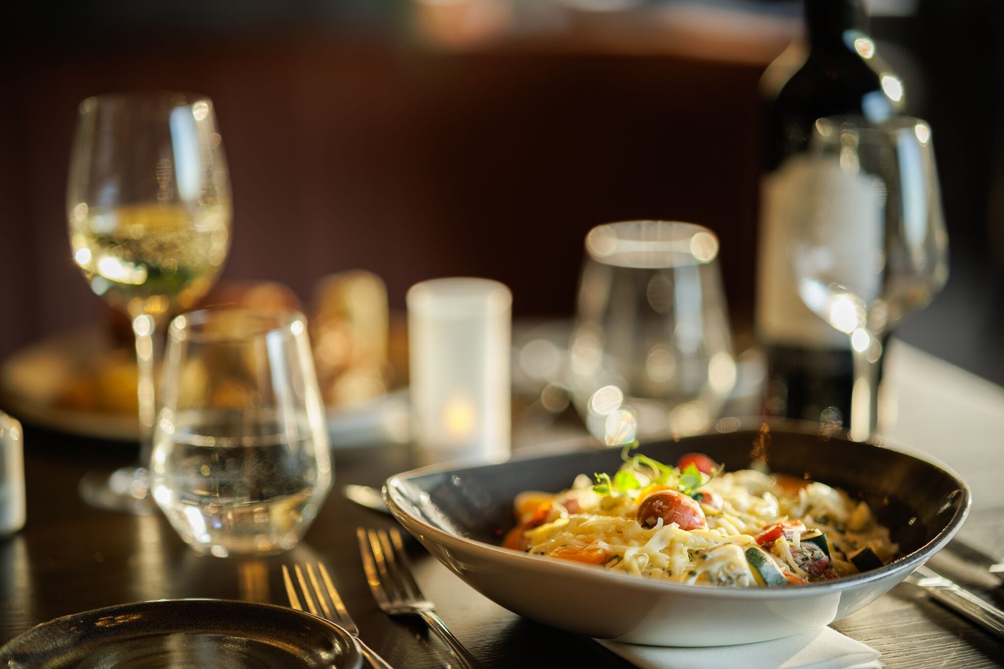 Une table à manger avec un saladier rempli de nourriture, des verres à vin et des couverts.