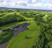 An aerial view of a golf course with multiple green areas, water bodies, and dense tree coverage.