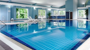 An indoor swimming pool with clear blue tiles, lounge chairs, and large windows offering views of greenery. - Hotel Woodstock, an Ascend Hotel Collection Member (Ennis)