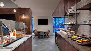 A modern kitchen with a central island, a dining area with chairs, and a buffet setup with various food items.