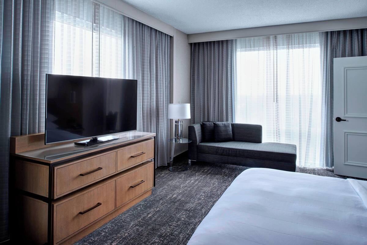 Een hotelkamer met een groot bed, een televisie op een houten dressoir, een bank en een bureau met een lamp.