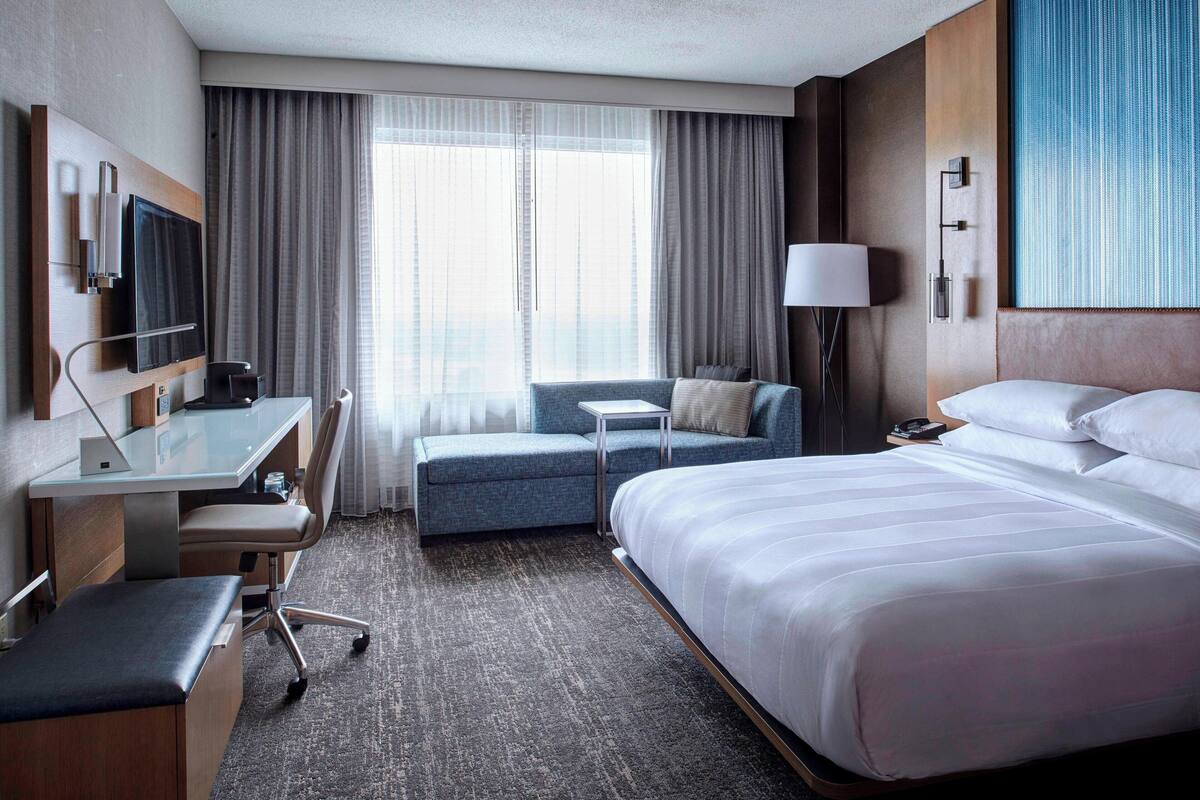 Hotelkamer met een groot bed, een bureau met stoel, een bank, een televisie en een raam met gordijnen.