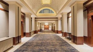 Corredor de hotel com piso em carpete, portas de madeira e teto com iluminação embutida.