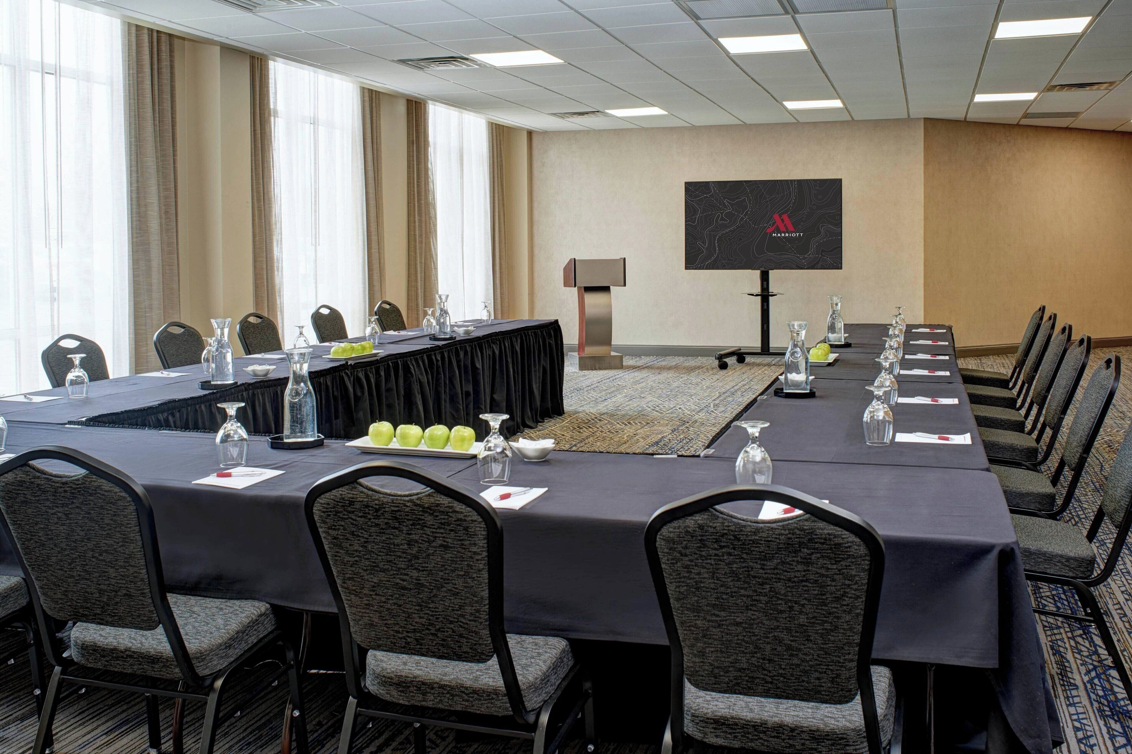 A conference room with a long table, chairs, a projector screen, and a podium.