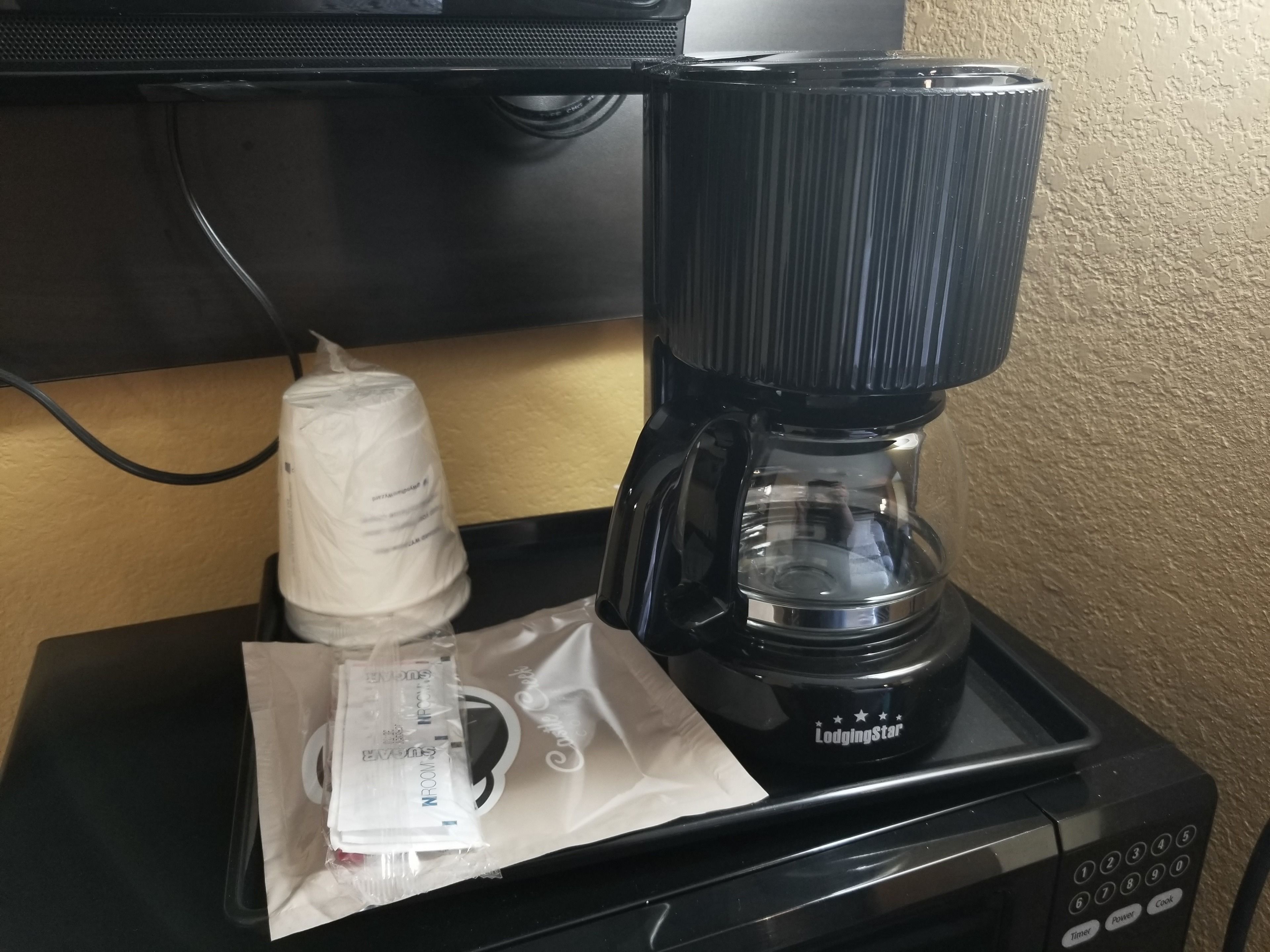 Une machine à café dotée d’un réservoir d’eau transparent, d’un compartiment pour les capsules de café et d’un câble d’alimentation branché.
